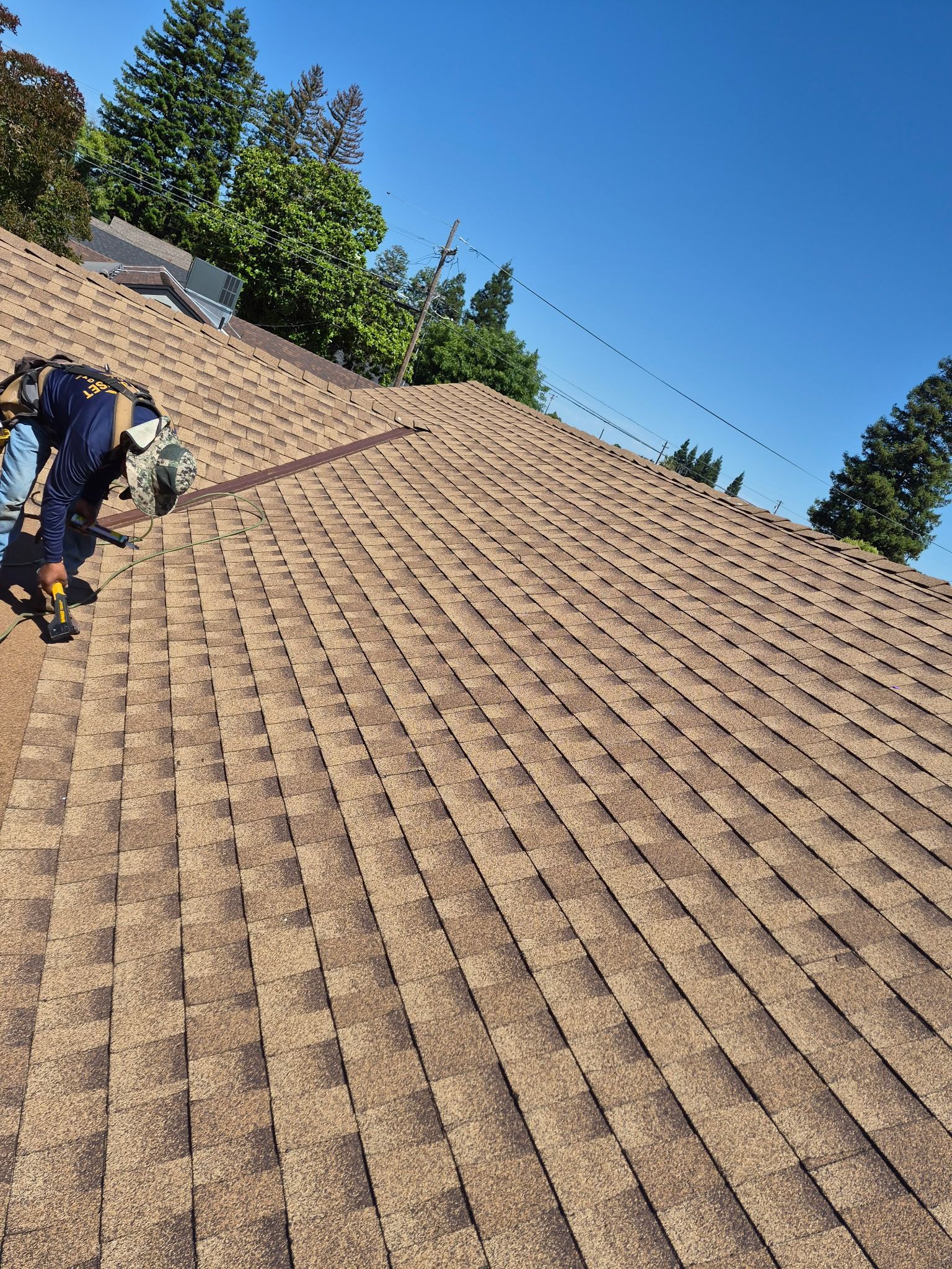 Roofers working on a tan shingle roof under a clear blue sky