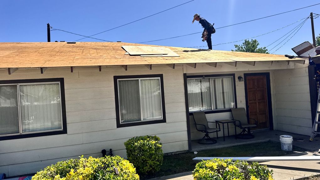 Single-story house with a damaged roof and a worker on top during repairs.