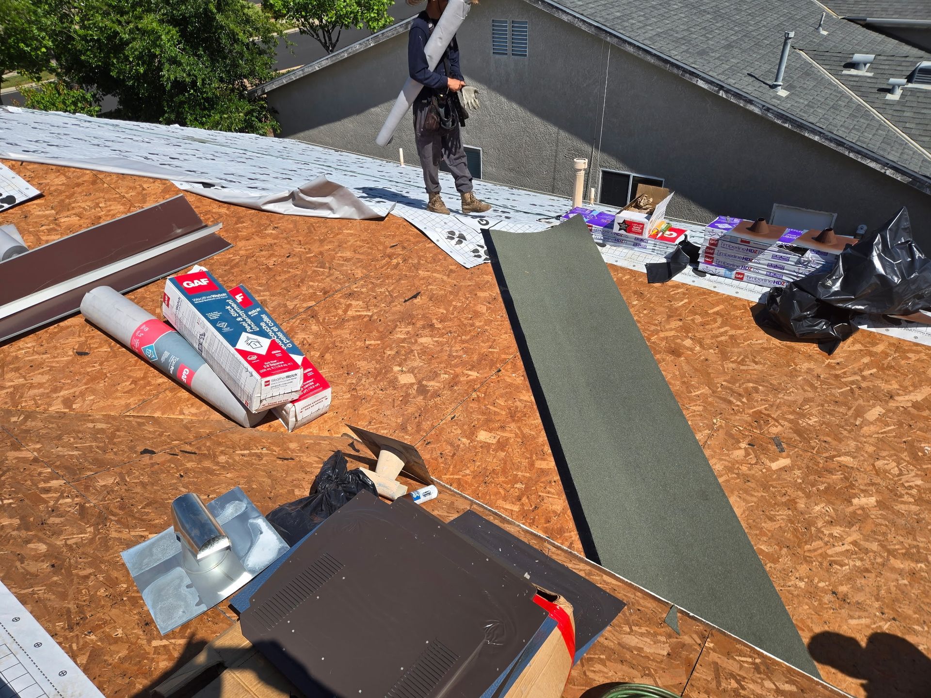 Roofer on a sloped roof with tools and shingles during repairs
