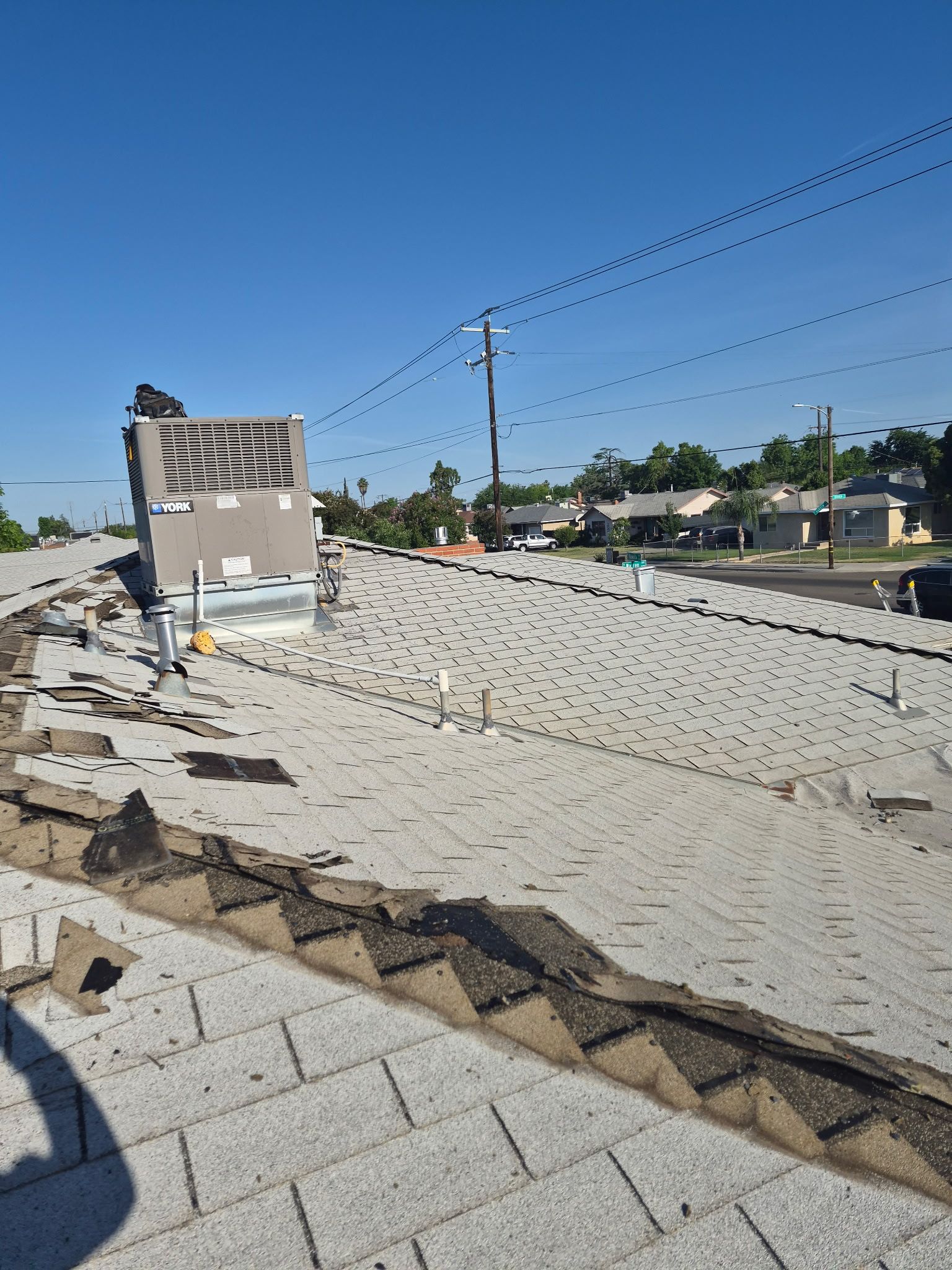 Rooftop with gray shingles, utility wires, and a clear blue sky over a suburban neighborhood
