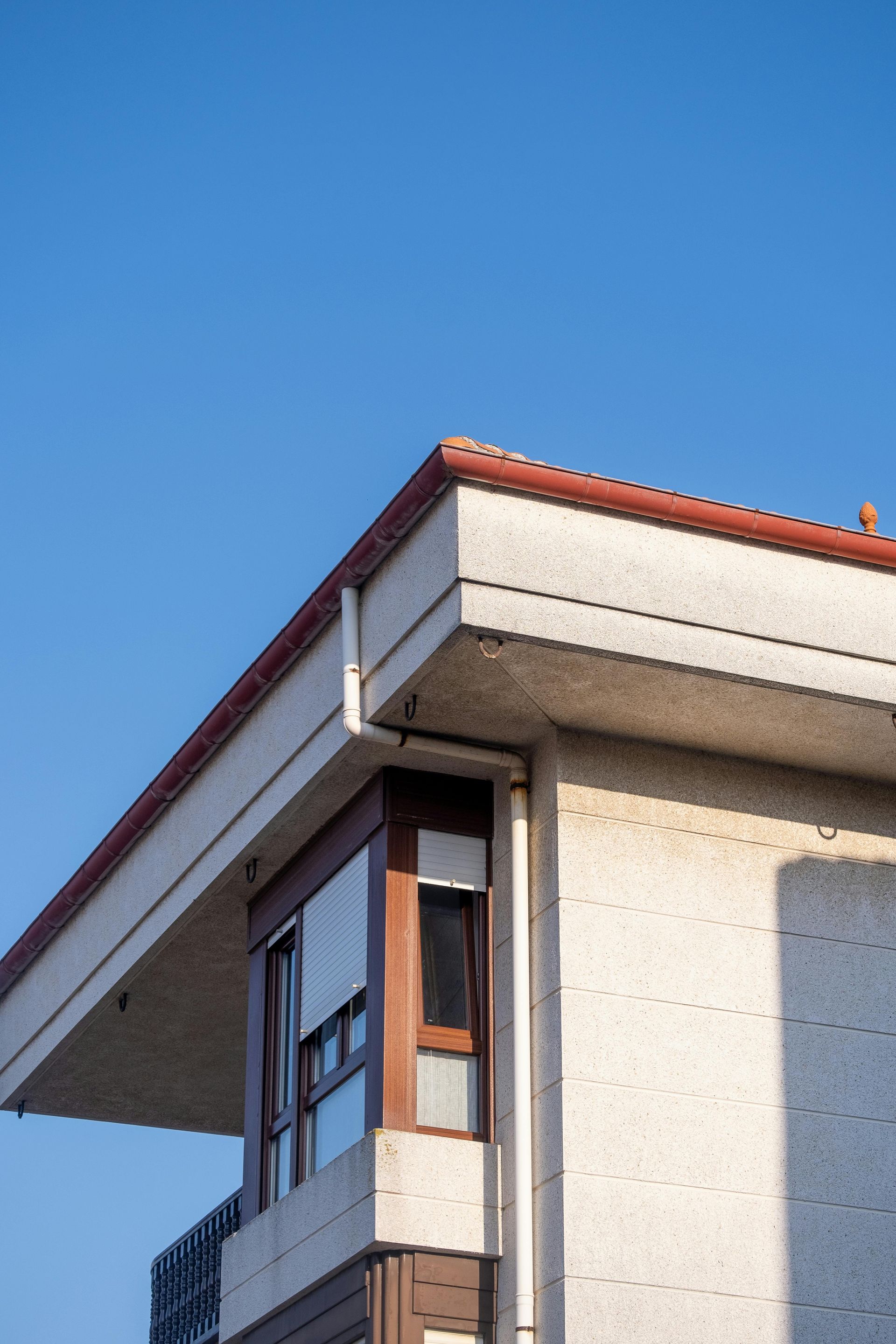 Corner of a modern building with a red-tiled roof against a clear blue sky