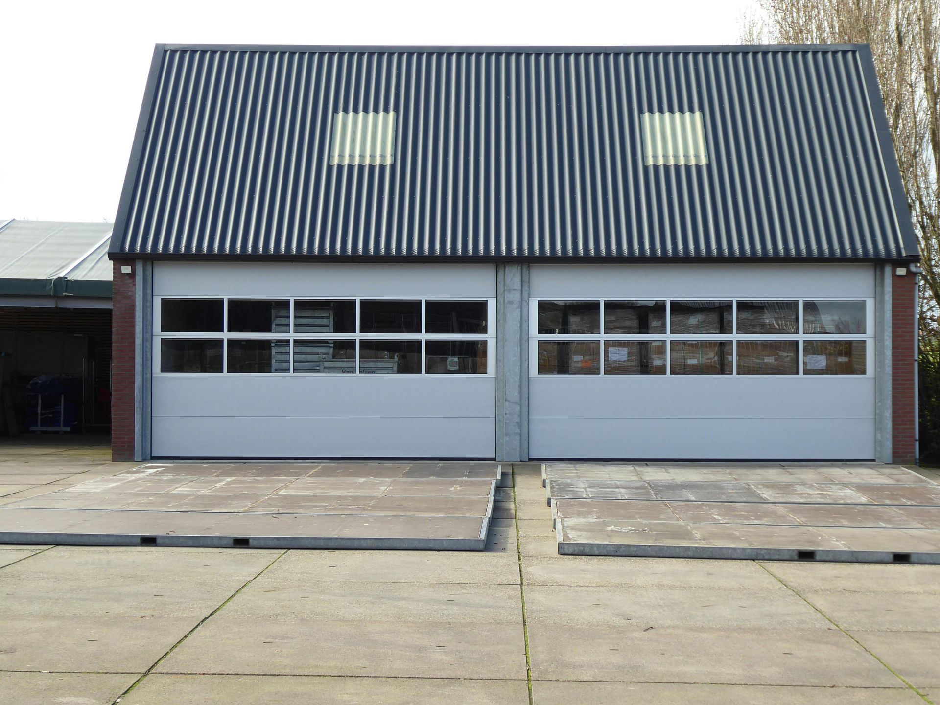 Front view of a gray building with a steep dark roof and two garage-style doors