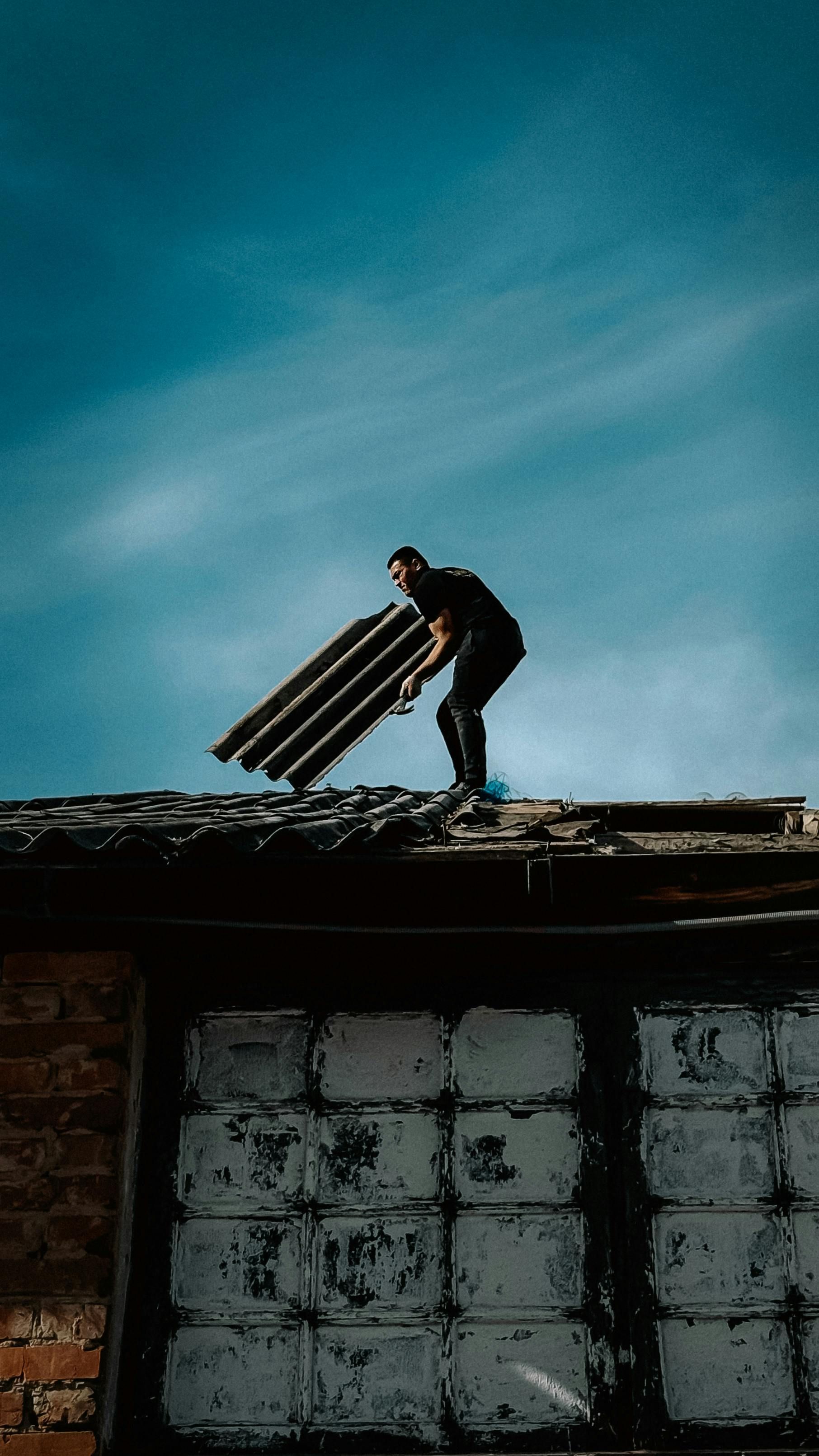 Worker on a rooftop carrying materials against a blue sky.