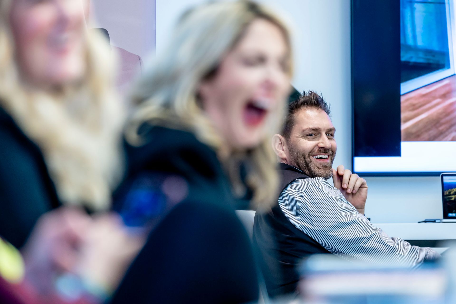 Mann am Schreibtisch mit Laptop und Telefon, klatscht in die Hände und lächelt in einem hellen Büro.