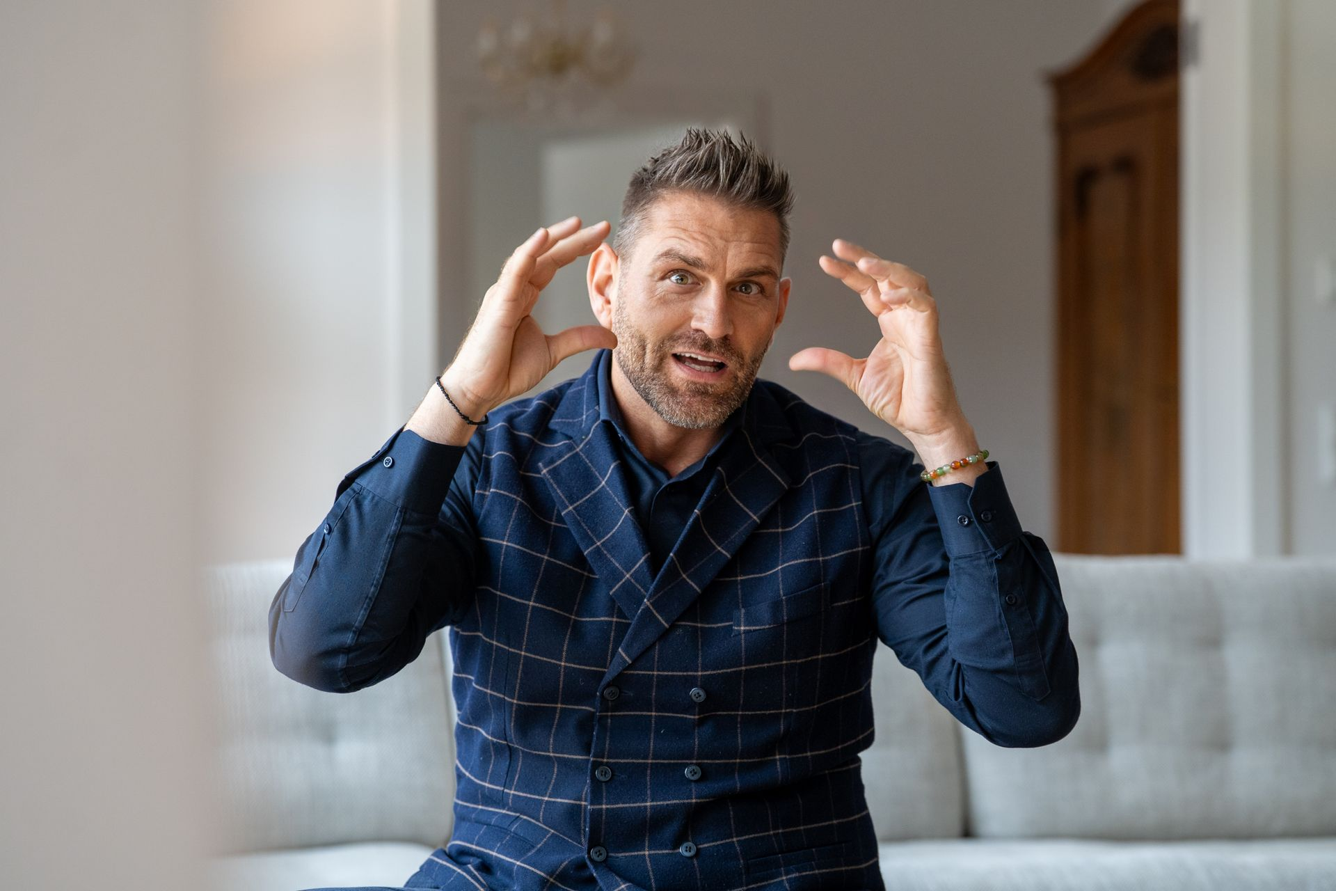 Ein Mann in einer blau gemusterten Weste gestikuliert überrascht in der Nähe seines Kopfes.