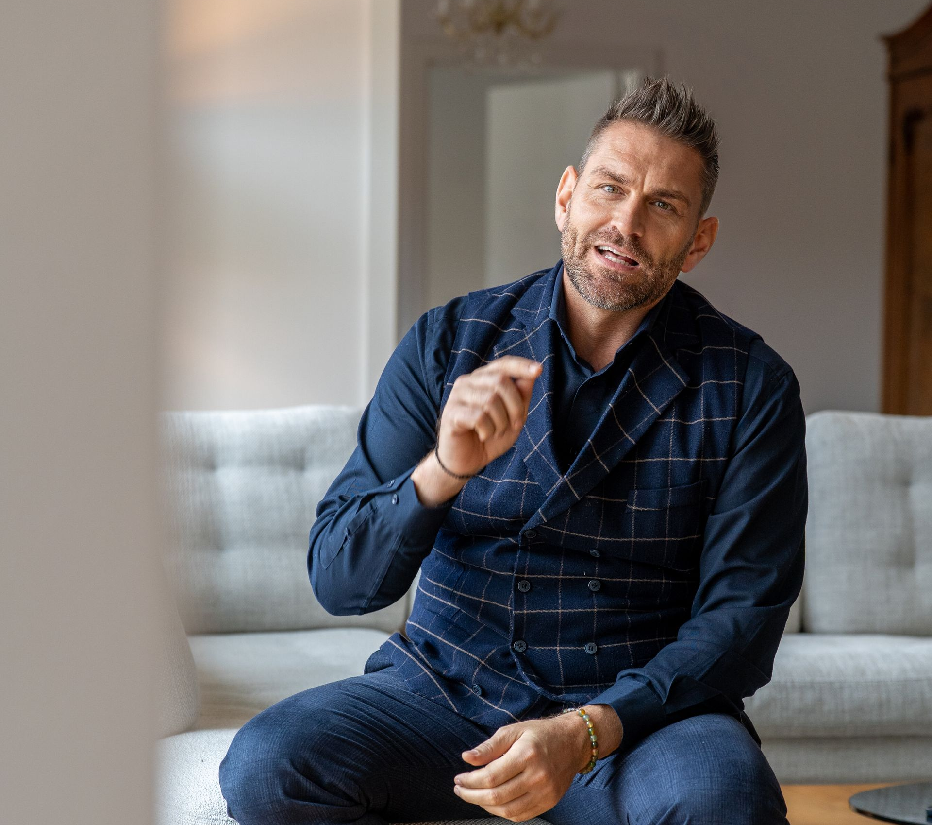 Mann im blauen Hemd klatscht in die Hände, Laptop, Smartphone auf dem Tisch.