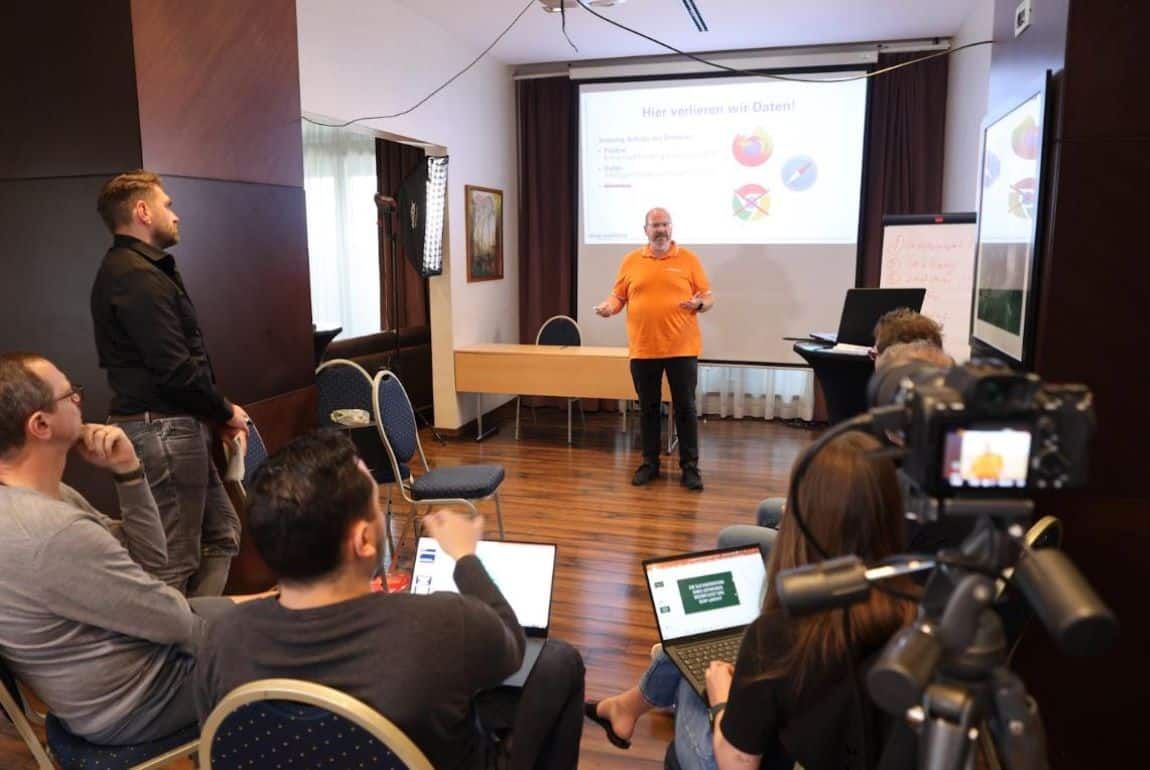 Ein Mann in einem orangefarbenen Hemd hält eine Präsentation vor einer Gruppe von Menschen