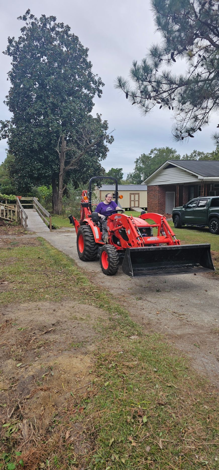 A backyard garden bed with dark mulch, several small green plants, and a dark-foliaged shrub, bordered by a white fence.