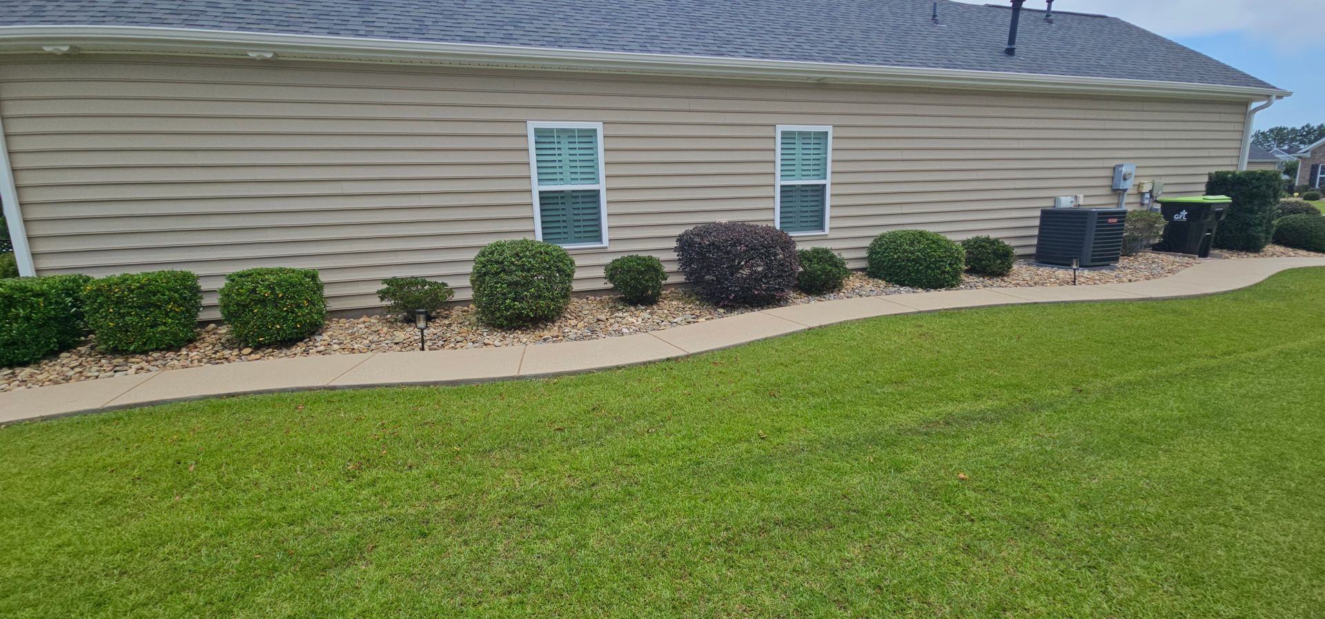 A brick house with a covered front porch, a well-manicured lawn, small shrubs, and a driveway with a truck in the distance.