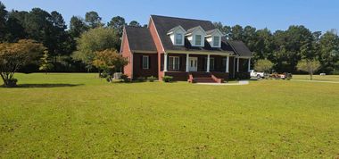 A dark, rounded shrub sits on a concrete driveway corner next to a brick house with an open garage and address 533.