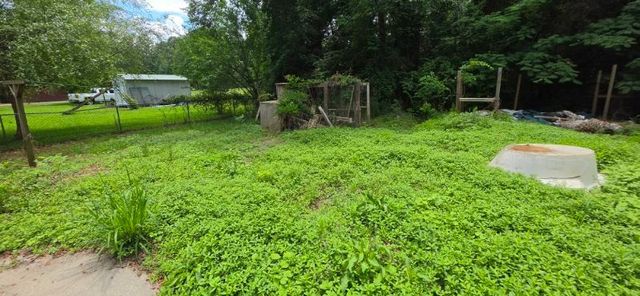 A backyard garden bed with dark mulch, several small green plants, and a dark-foliaged shrub, bordered by a white fence.