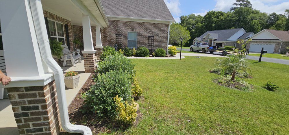 A porch view of a brick house with a front lawn, landscaping shrubs, and a driveway with a truck in a suburban neighborhood.
