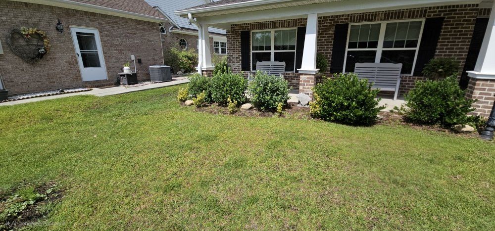 A brick house with a front porch, green lawn, and neatly trimmed landscaping shrubs.