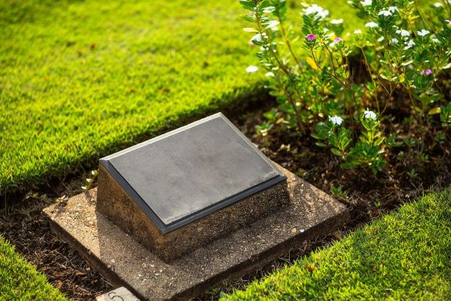 There is a gravestone in the middle of the grass in a cemetery.