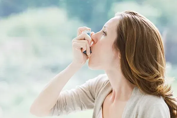 A woman is using an inhaler to treat her asthma.