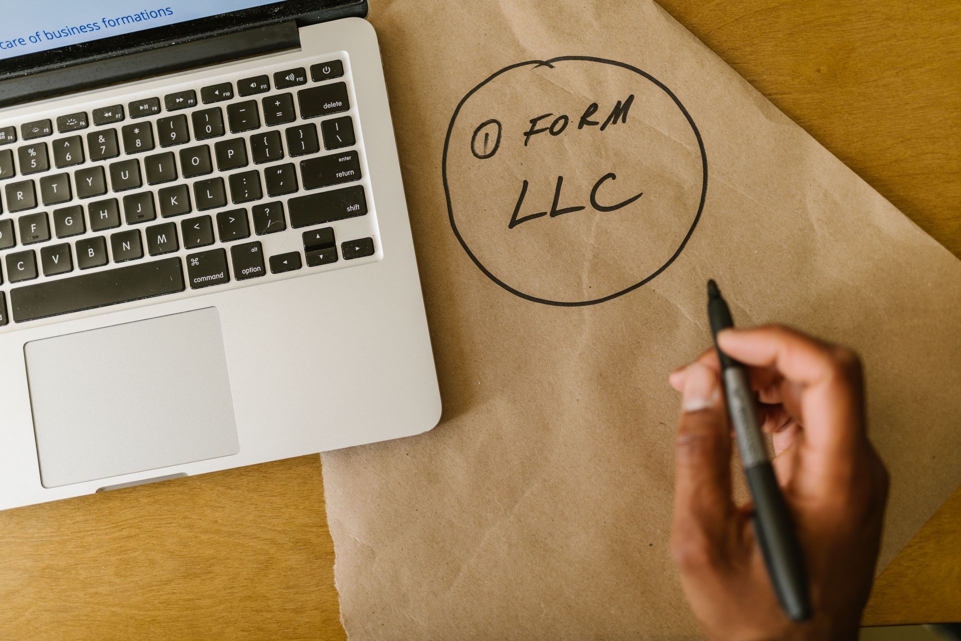 Hand writing “I FORM LLC” on brown paper beside a laptop