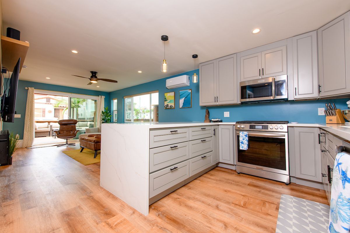 A kitchen with gray cabinets , stainless steel appliances , and a large island in the middle of the room.