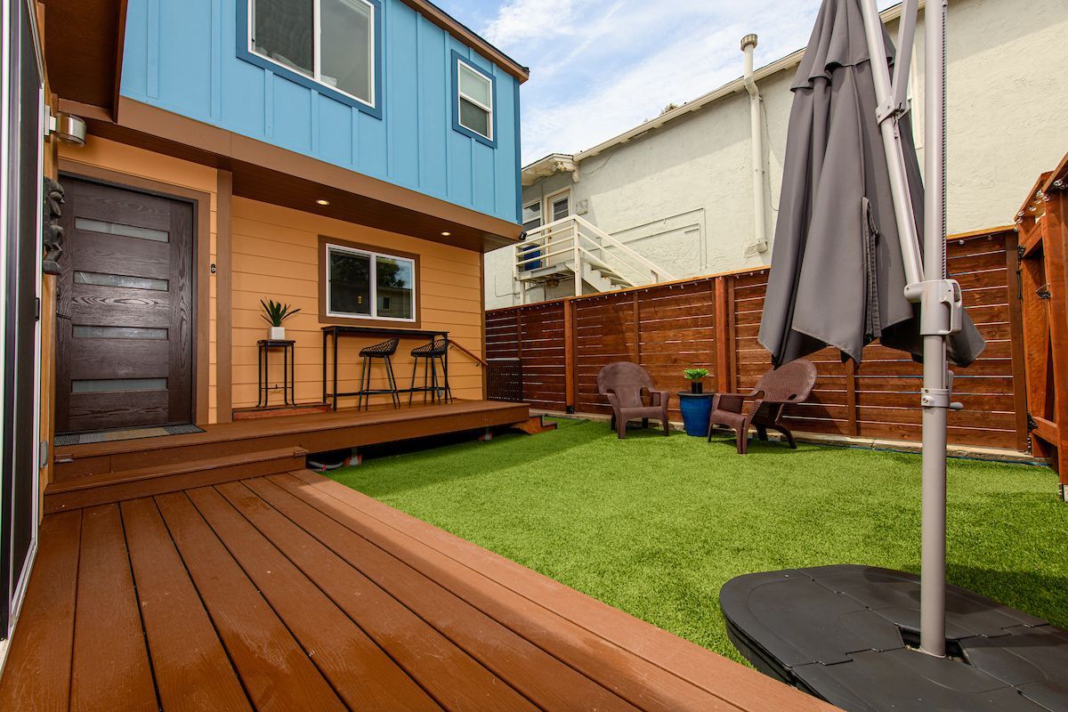 A backyard with a wooden deck , umbrella , chairs and a table.