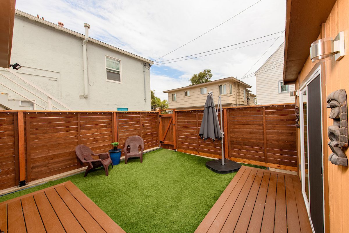 A backyard with a wooden deck , chairs and umbrella.