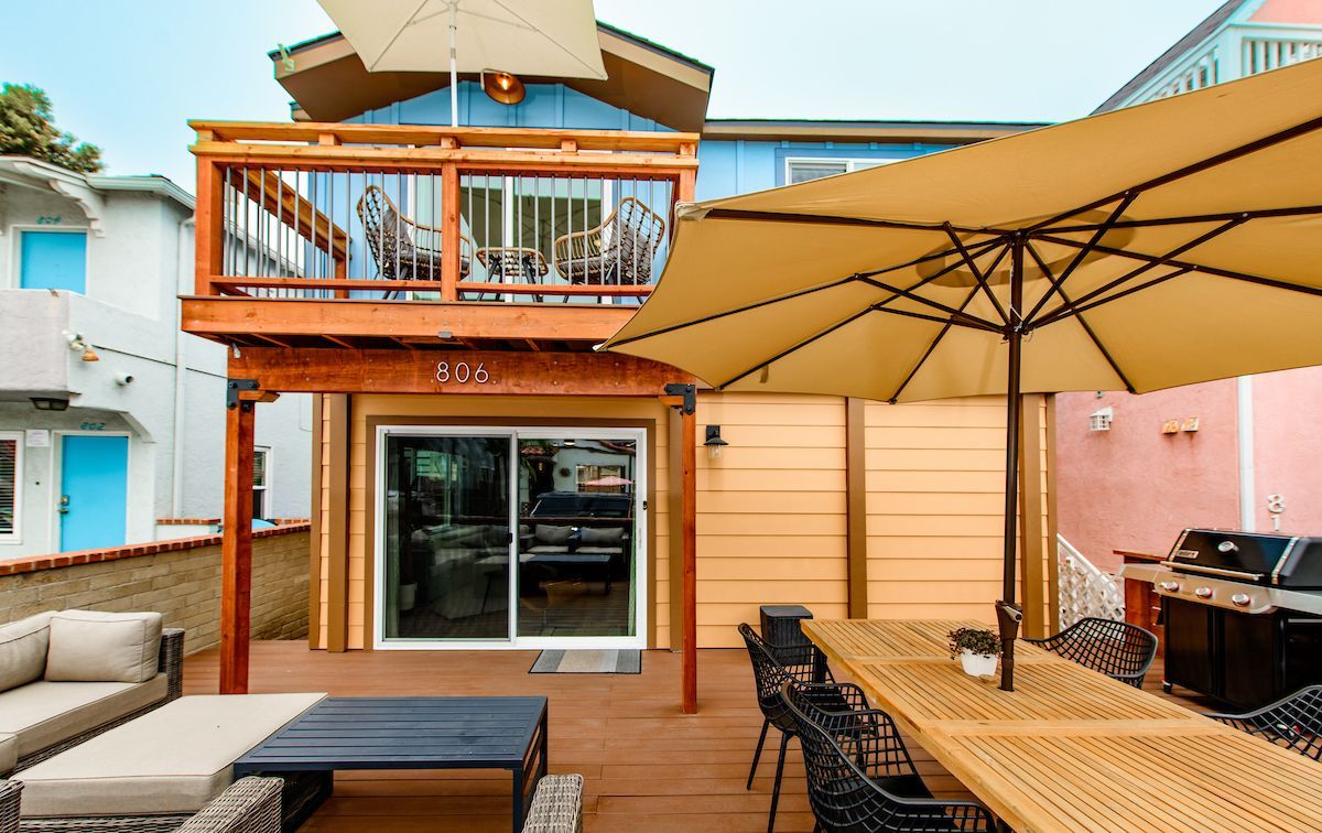 A patio with a table and chairs and umbrellas in front of a house.