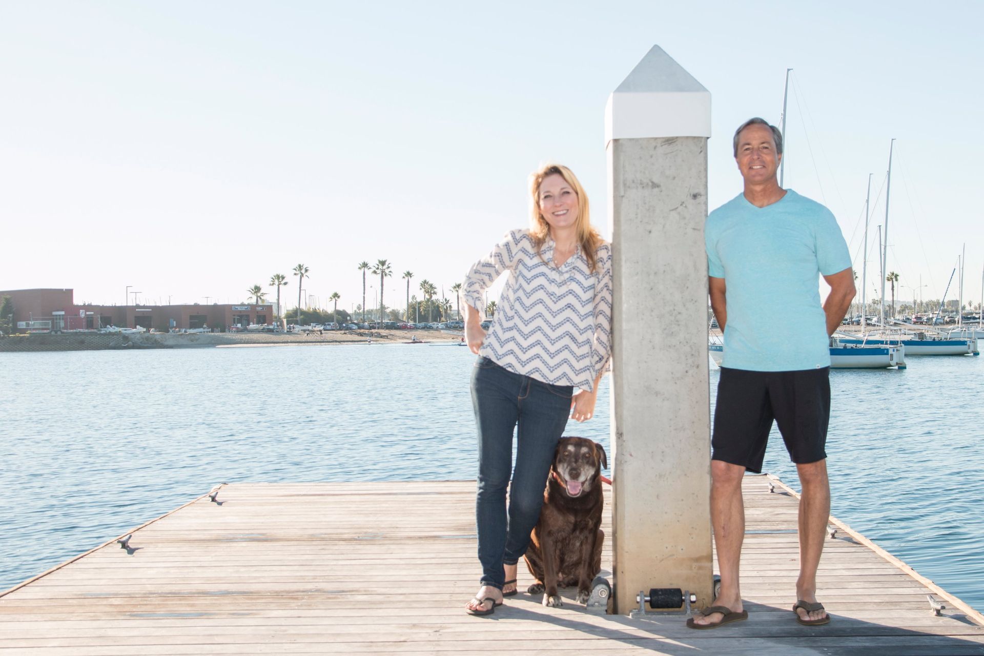 A man and a woman are standing on a dock with a dog.