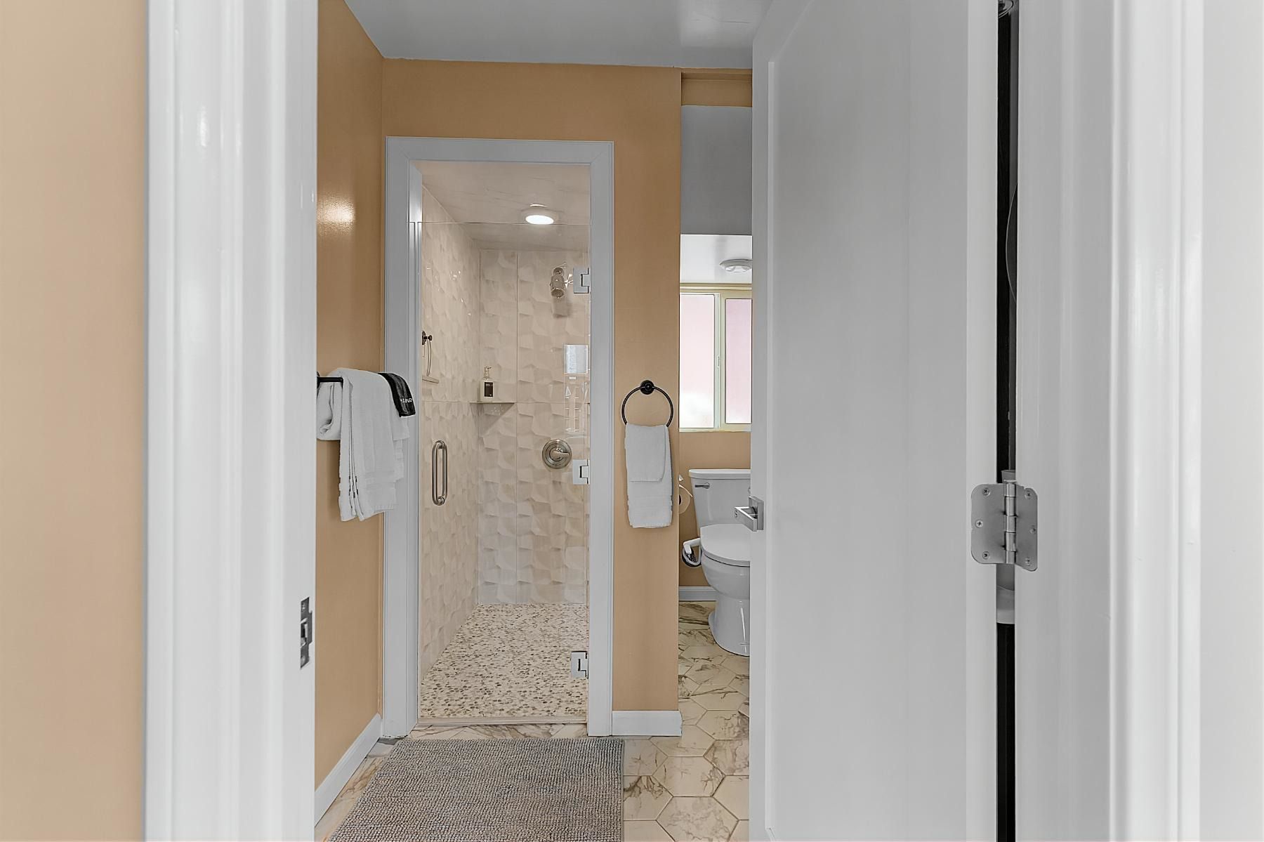 A bathroom with a walk in shower , toilet , and towel rack.