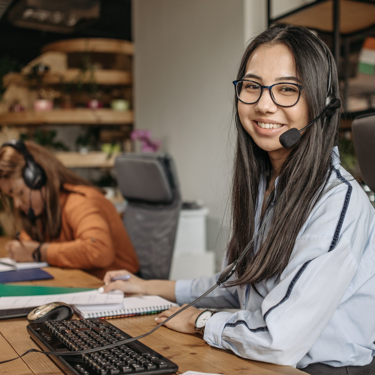A woman wearing a headset is sitting at a desk with a keyboard.