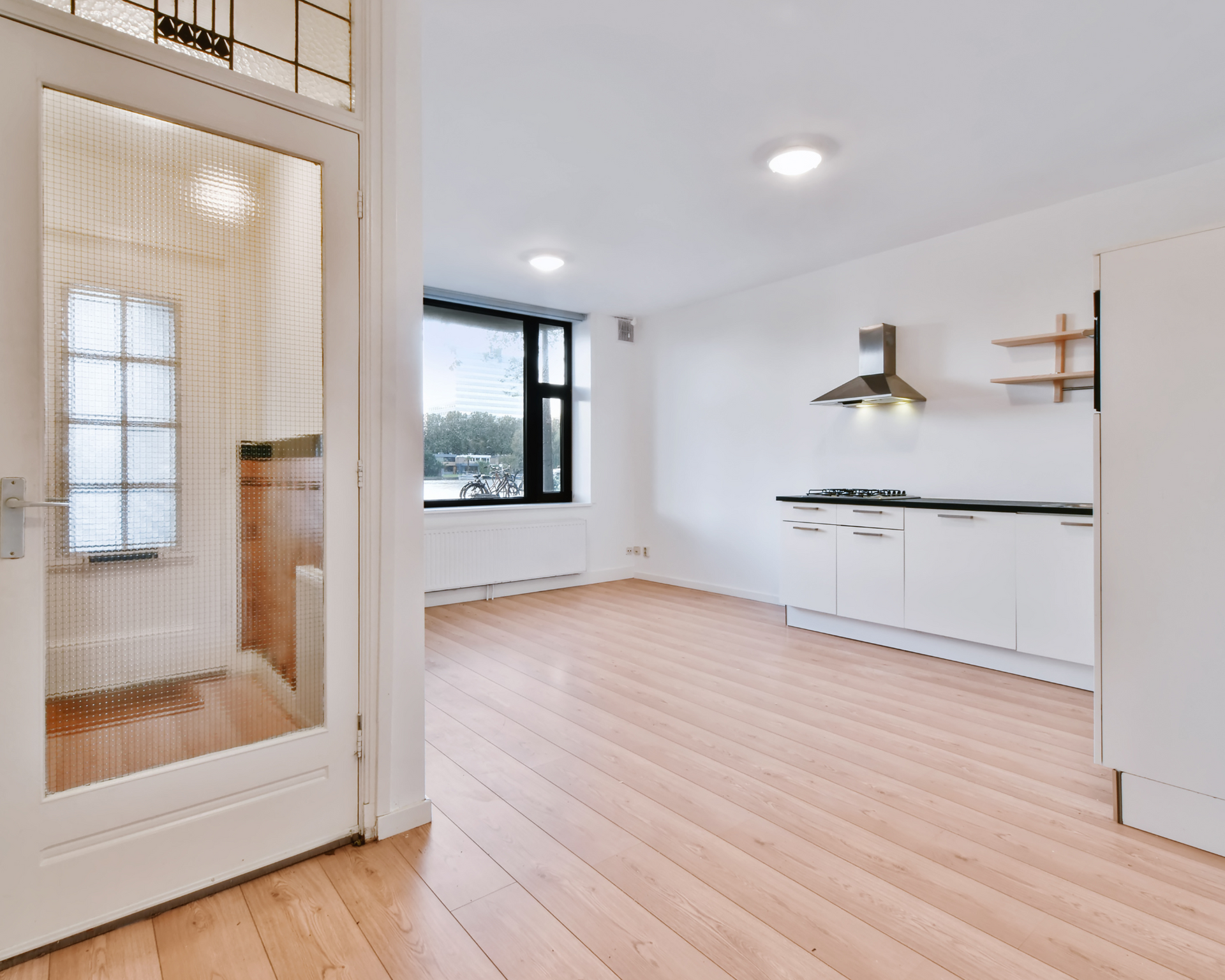 An empty room with hardwood floors and white cabinets