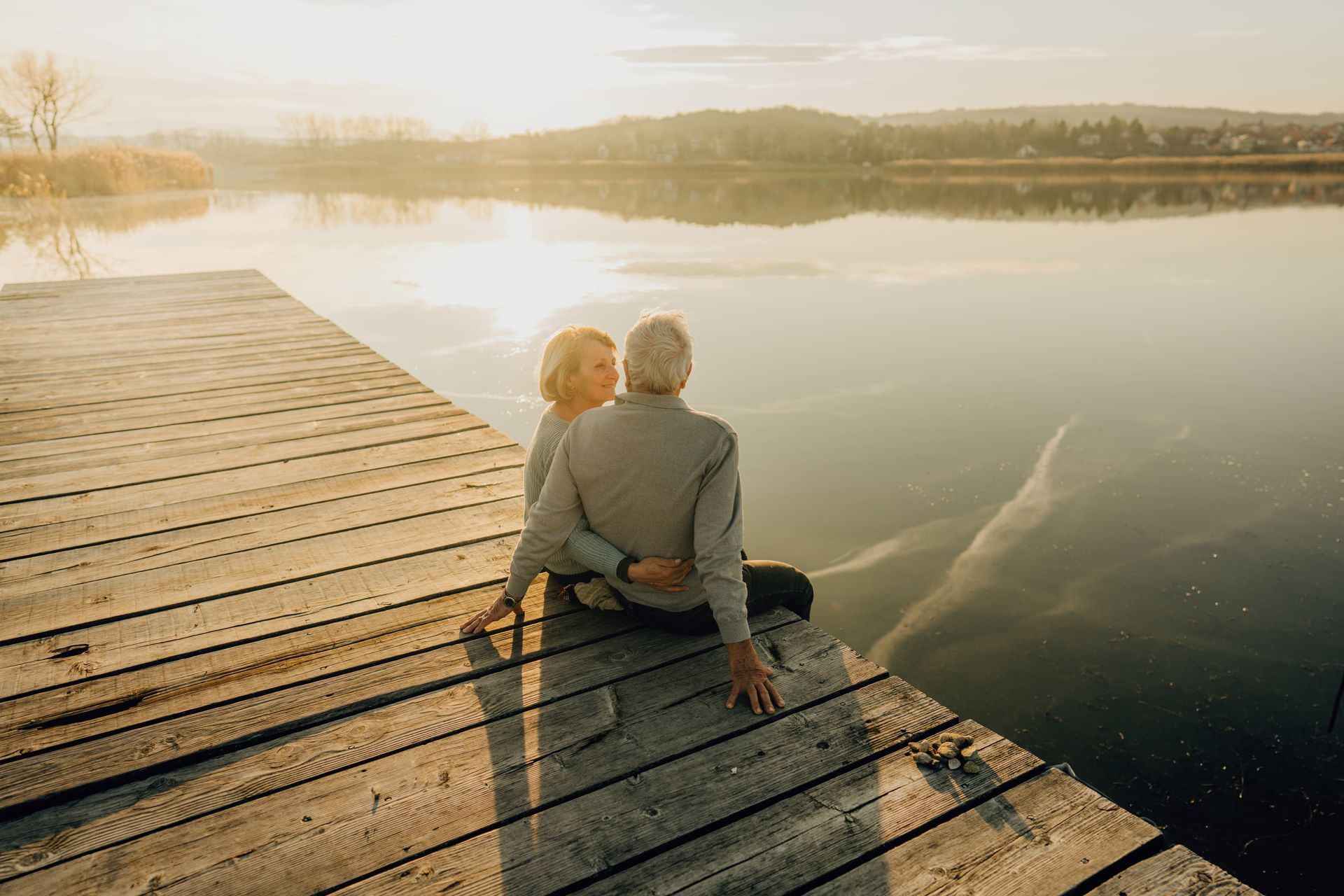 An elderly couple is sitting on a dock overlooking a lake.