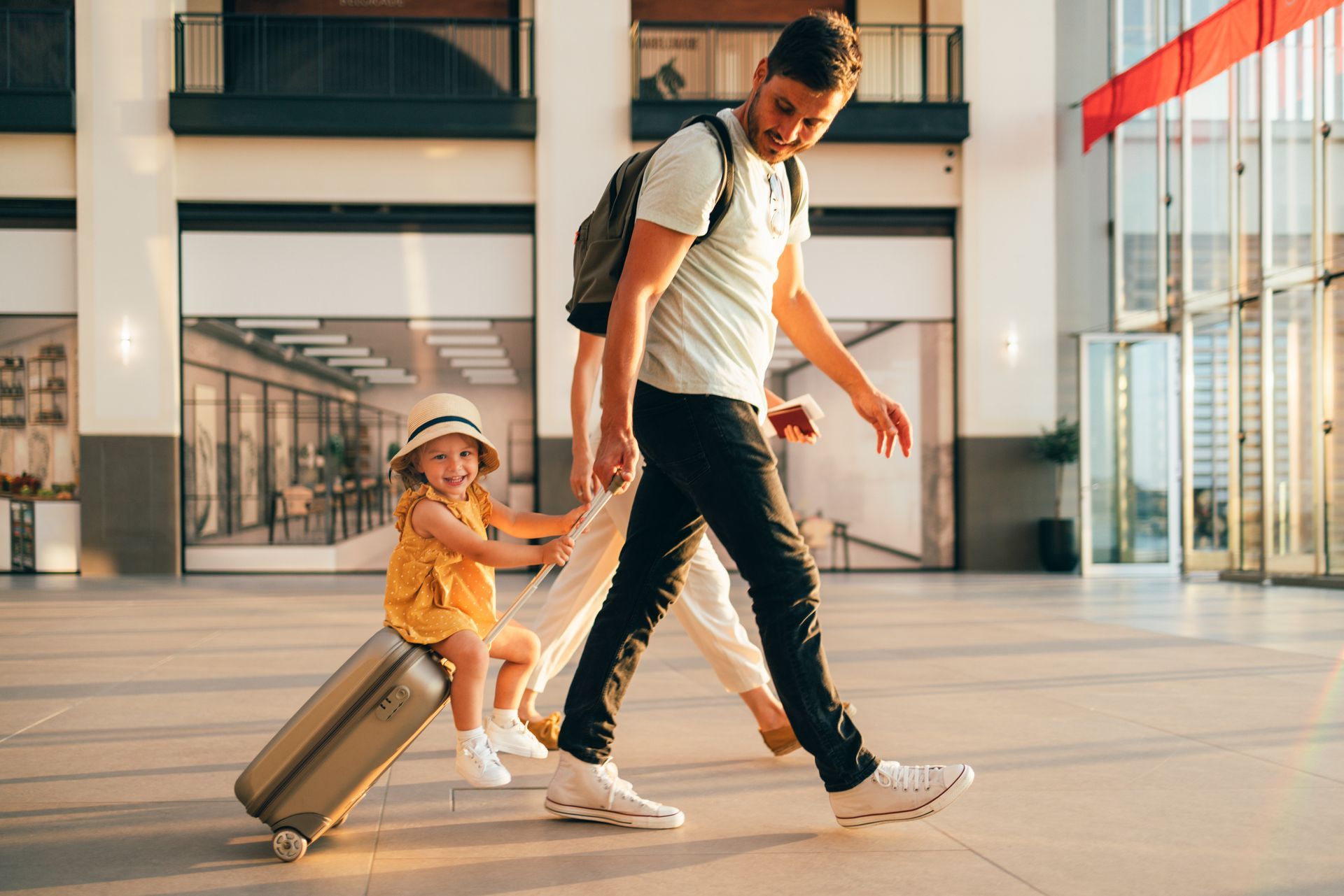 A man and a little girl are pulling a suitcase at an airport.