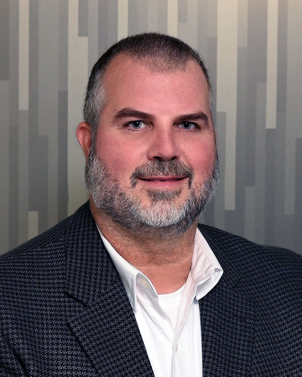 A man with a beard is wearing a suit and white shirt.