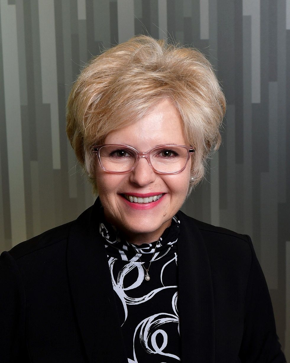 A woman wearing glasses and a black jacket is smiling for the camera.