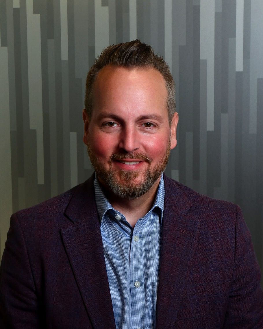 A man with a beard is wearing a purple jacket and a blue shirt.