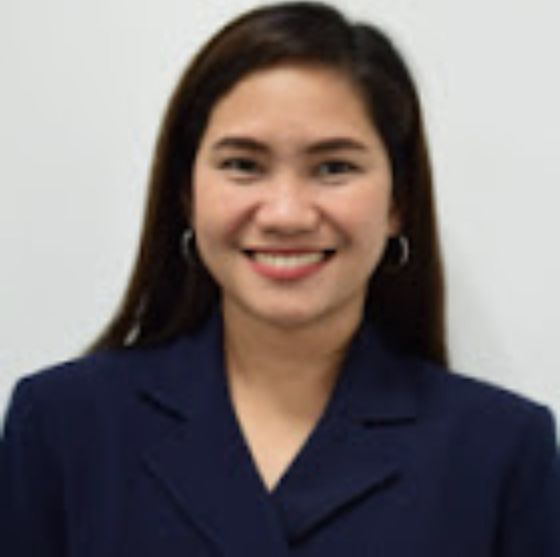 A woman wearing a blue jacket and earrings smiles for the camera.