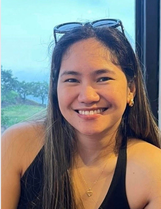 A woman wearing a blue jacket and earrings smiles for the camera.