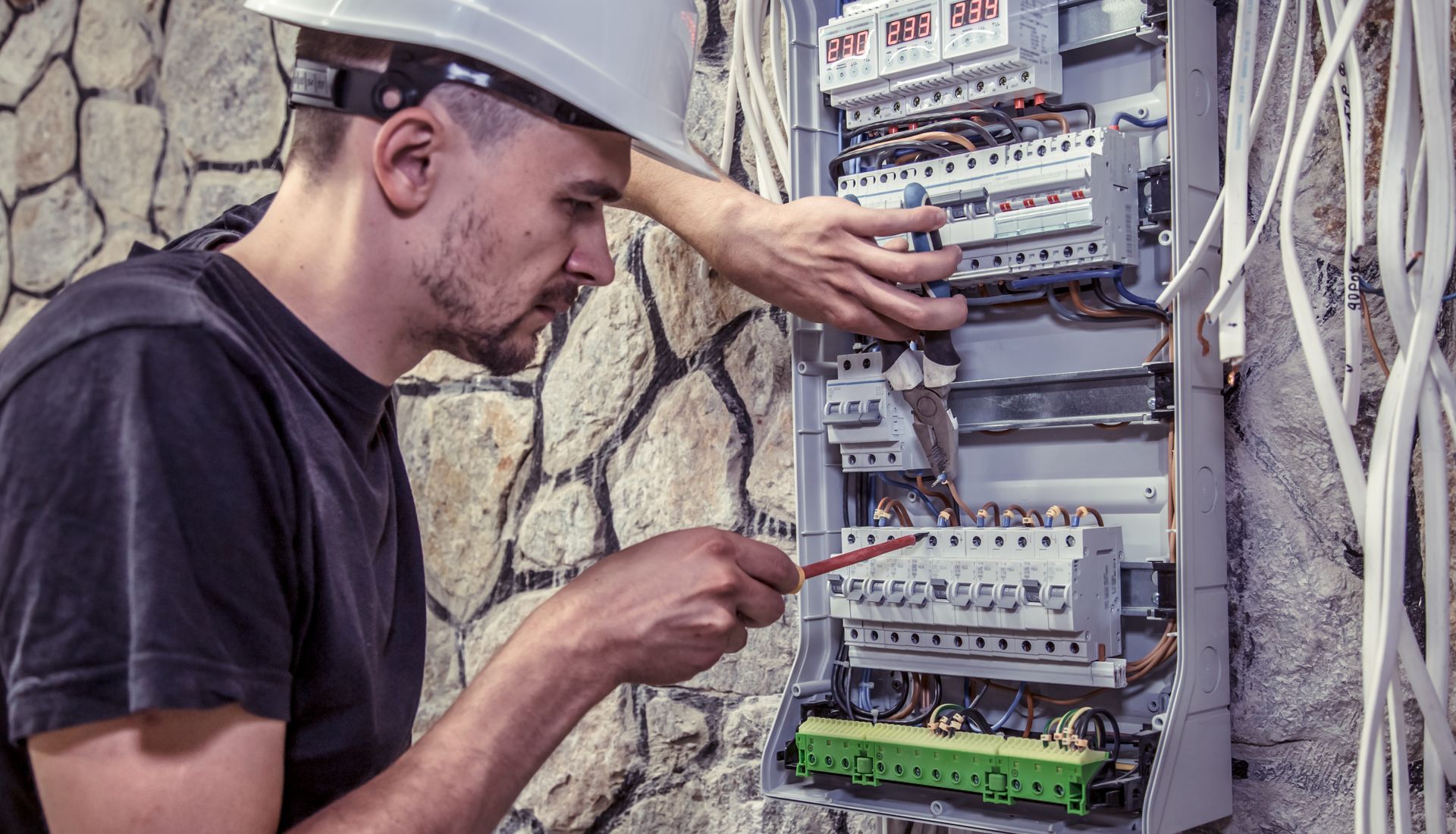 A male electrician checks the breakers of a breaker box installed on a wall.