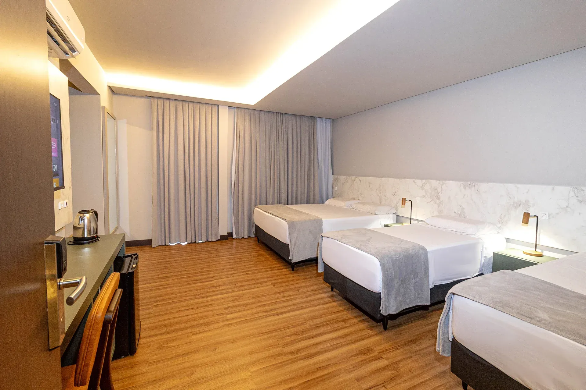 Um quarto de hotel com três camas e uma escrivaninha.