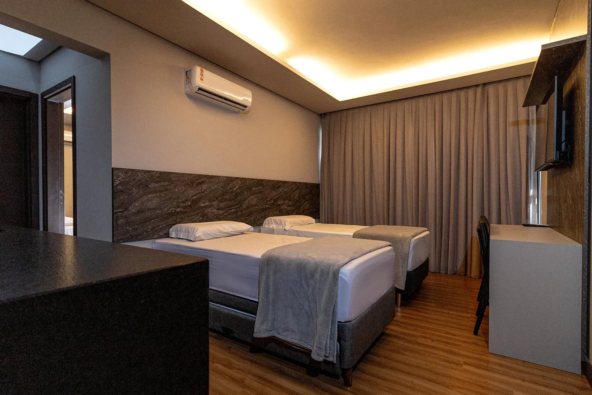 Um quarto de hotel com duas camas, uma escrivaninha e uma televisão.