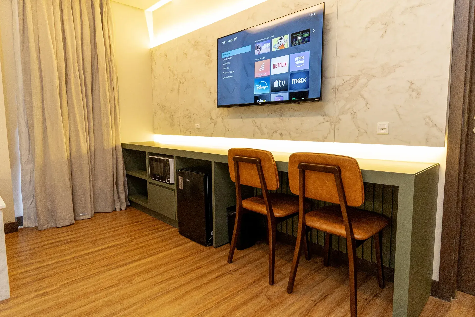 Um quarto de hotel com uma mesa, cadeiras e uma TV de tela plana na parede.