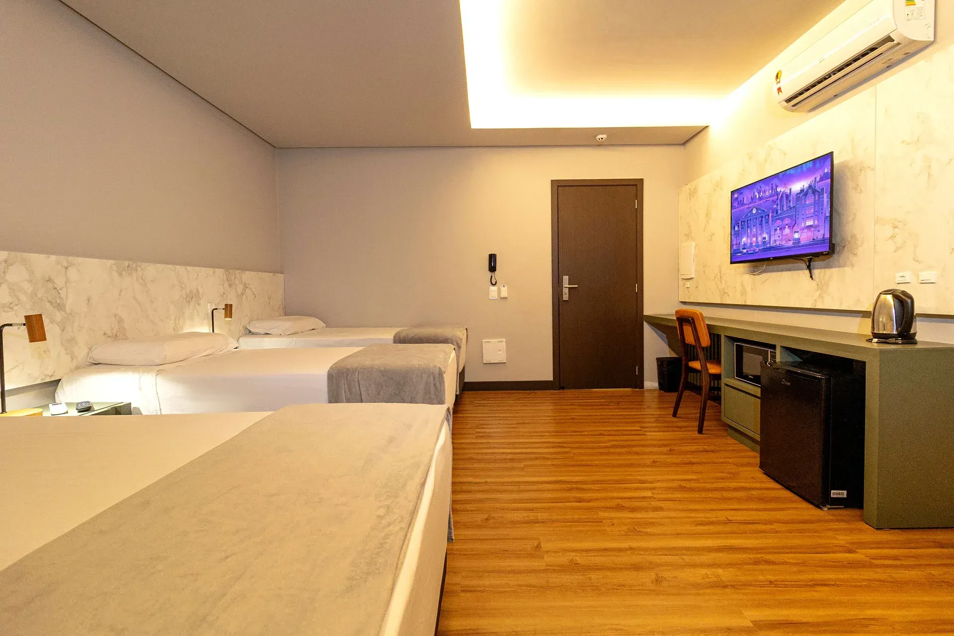 Um quarto de hotel com três camas, uma escrivaninha e uma TV de tela plana.