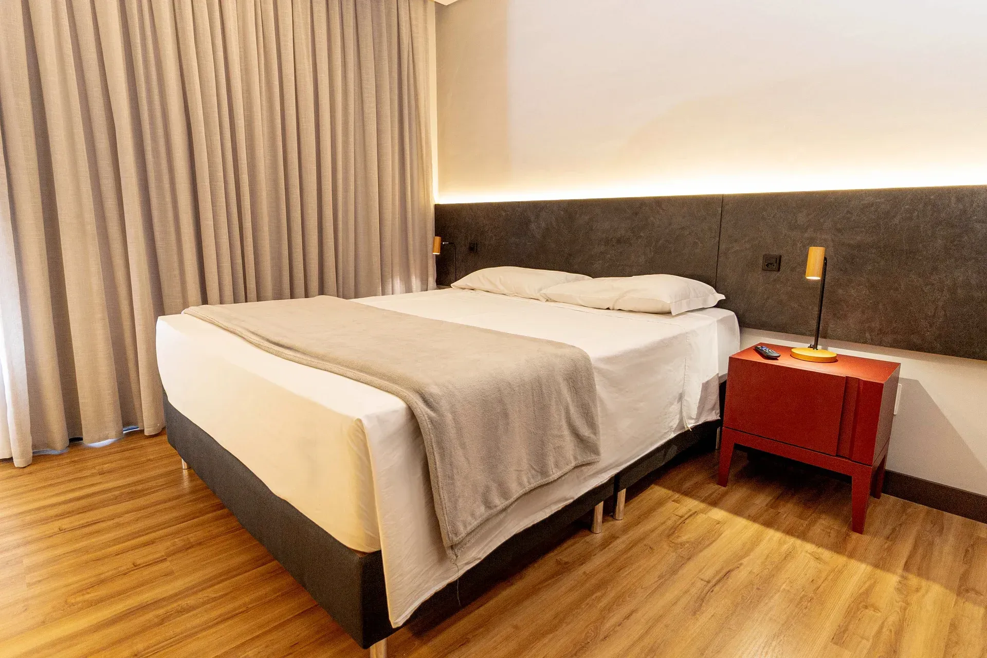 Um quarto de hotel com uma cama, mesa de cabeceira e cortinas.