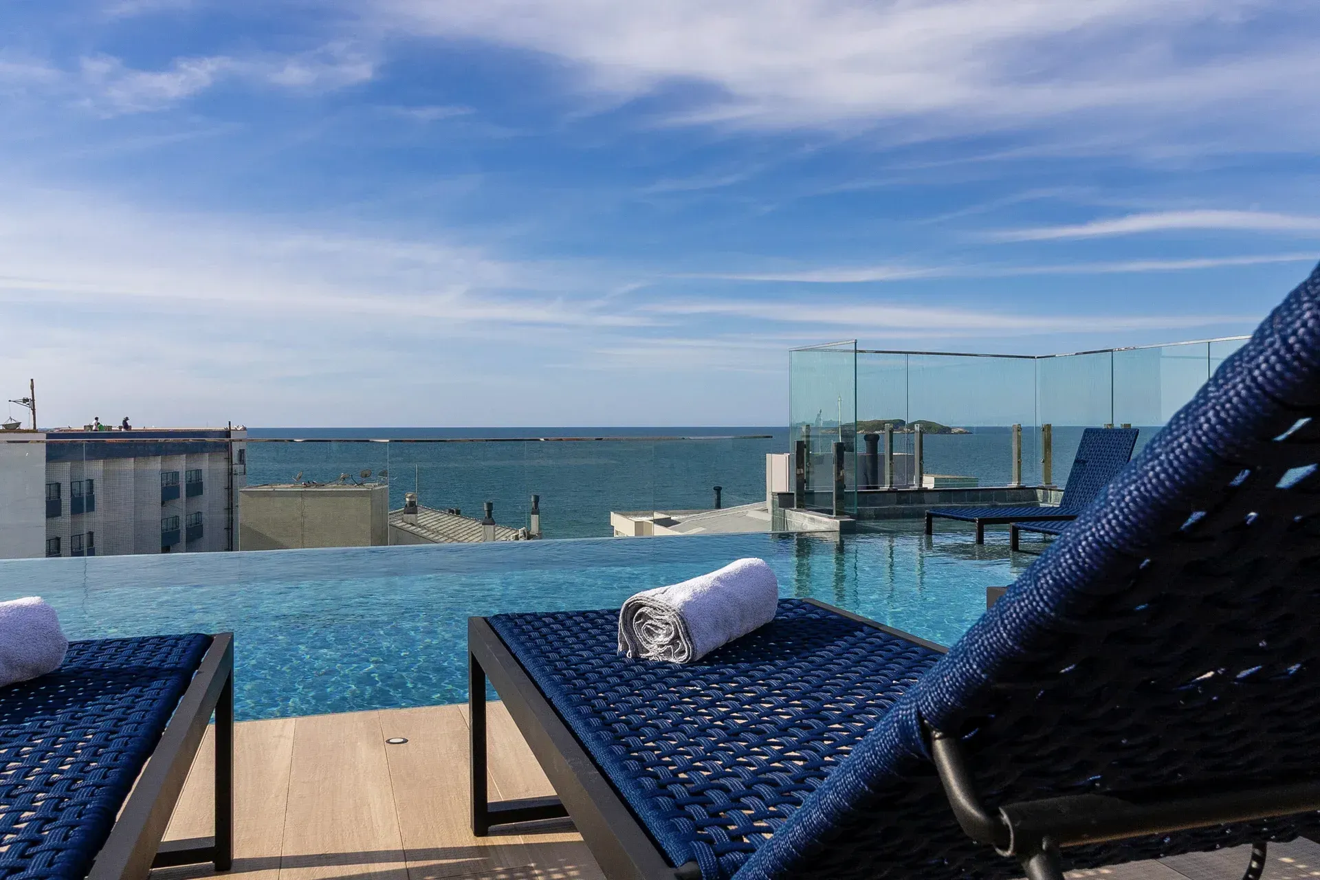 Duas espreguiçadeiras estão ao lado de uma piscina infinita com vista para o oceano.