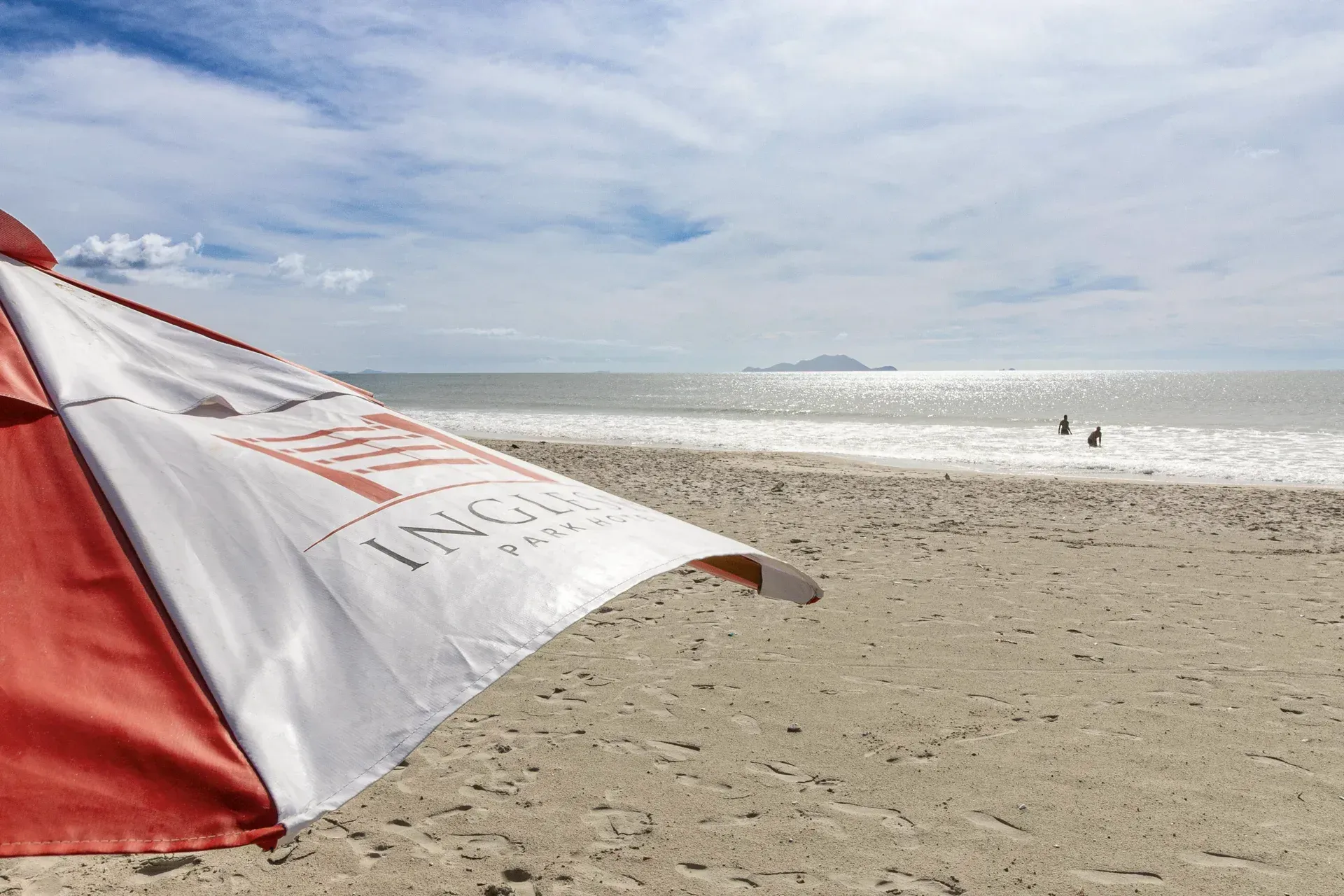 Um guarda-chuva vermelho e branco está balançando ao vento em uma praia.