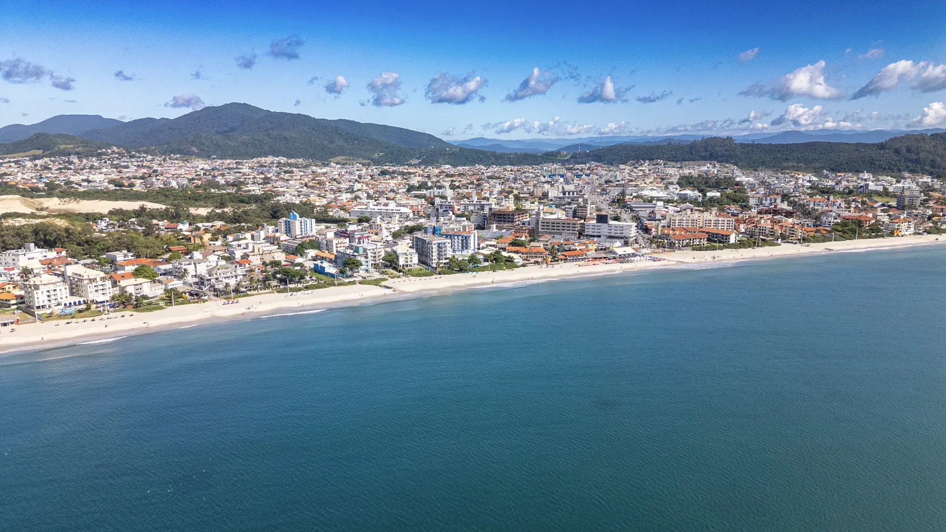 Uma vista aérea de uma cidade e uma praia com montanhas ao fundo.