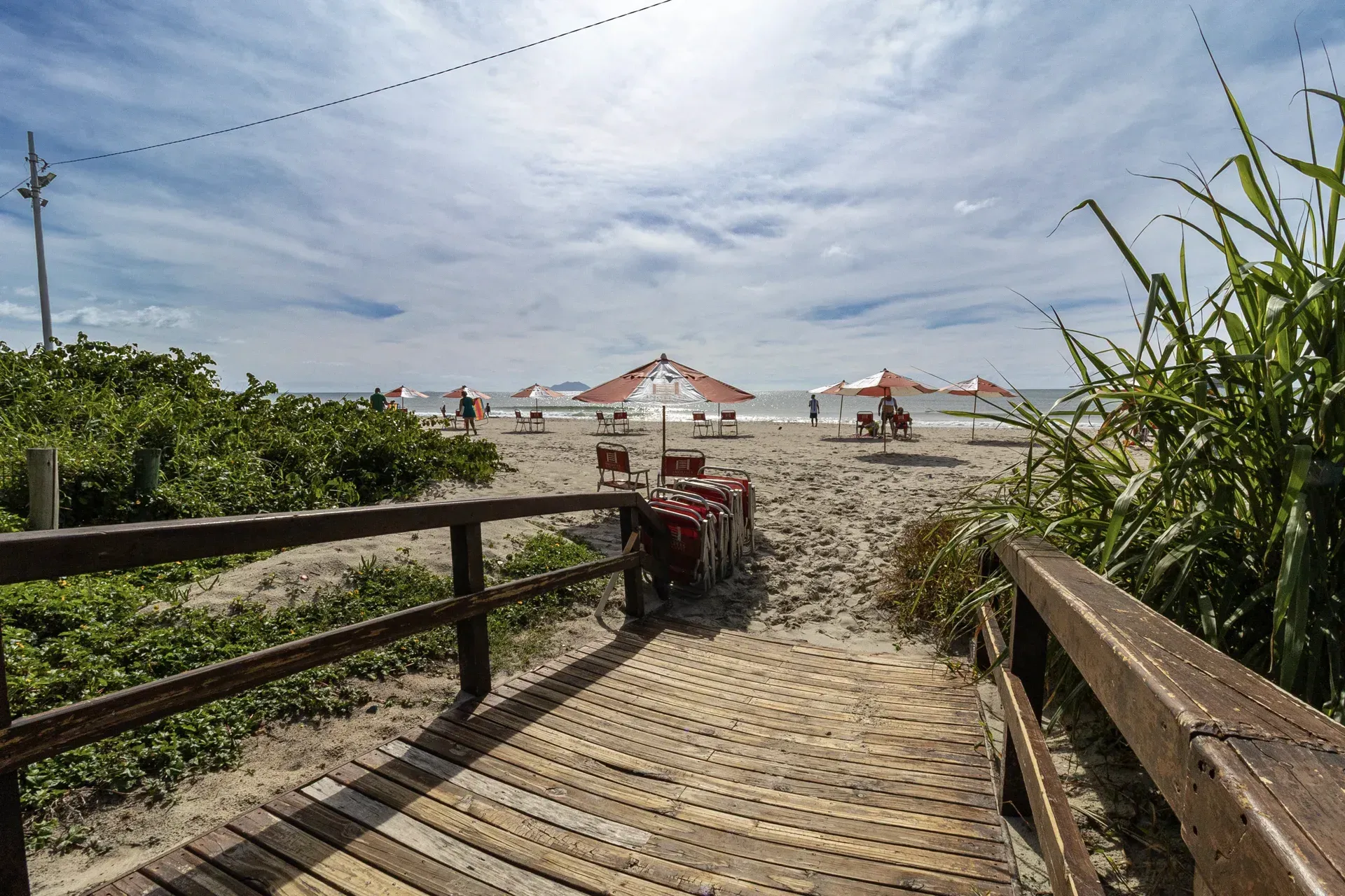 Uma passarela de madeira que leva a uma praia com guarda-sóis e cadeiras