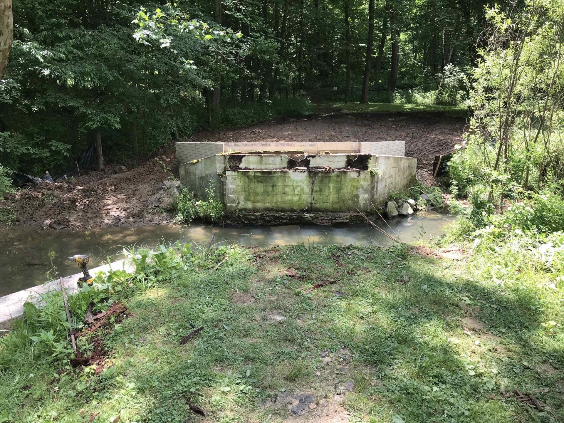 A concrete structure is sitting next to a river in the woods.