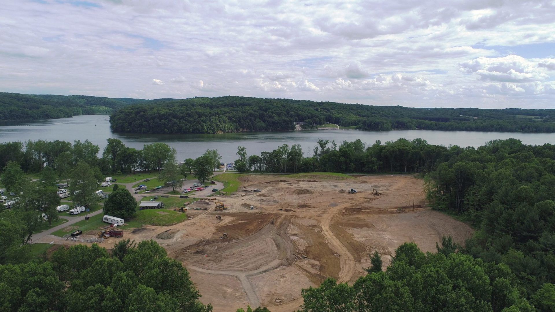 An aerial view of a construction site next to a lake surrounded by trees.