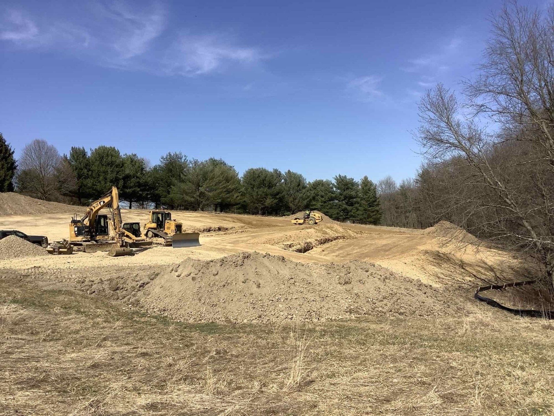 A group of construction vehicles are working on a dirt field.