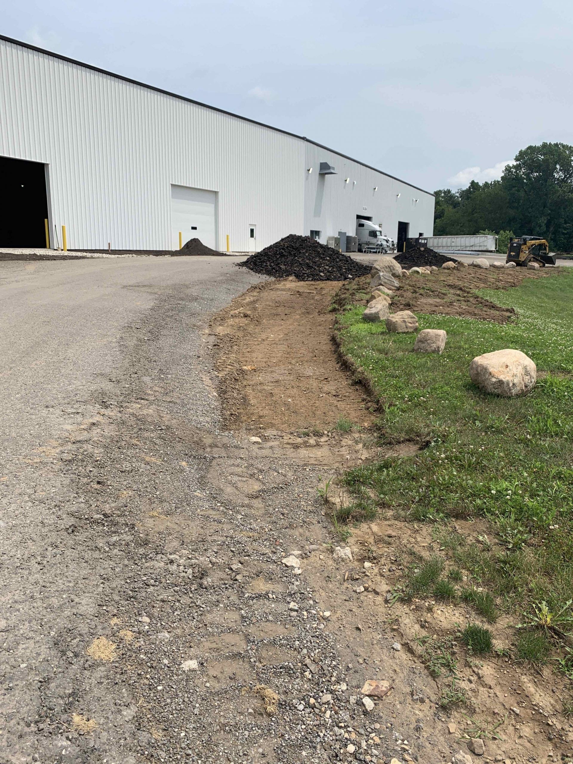 A large white building is being built next to a gravel road.