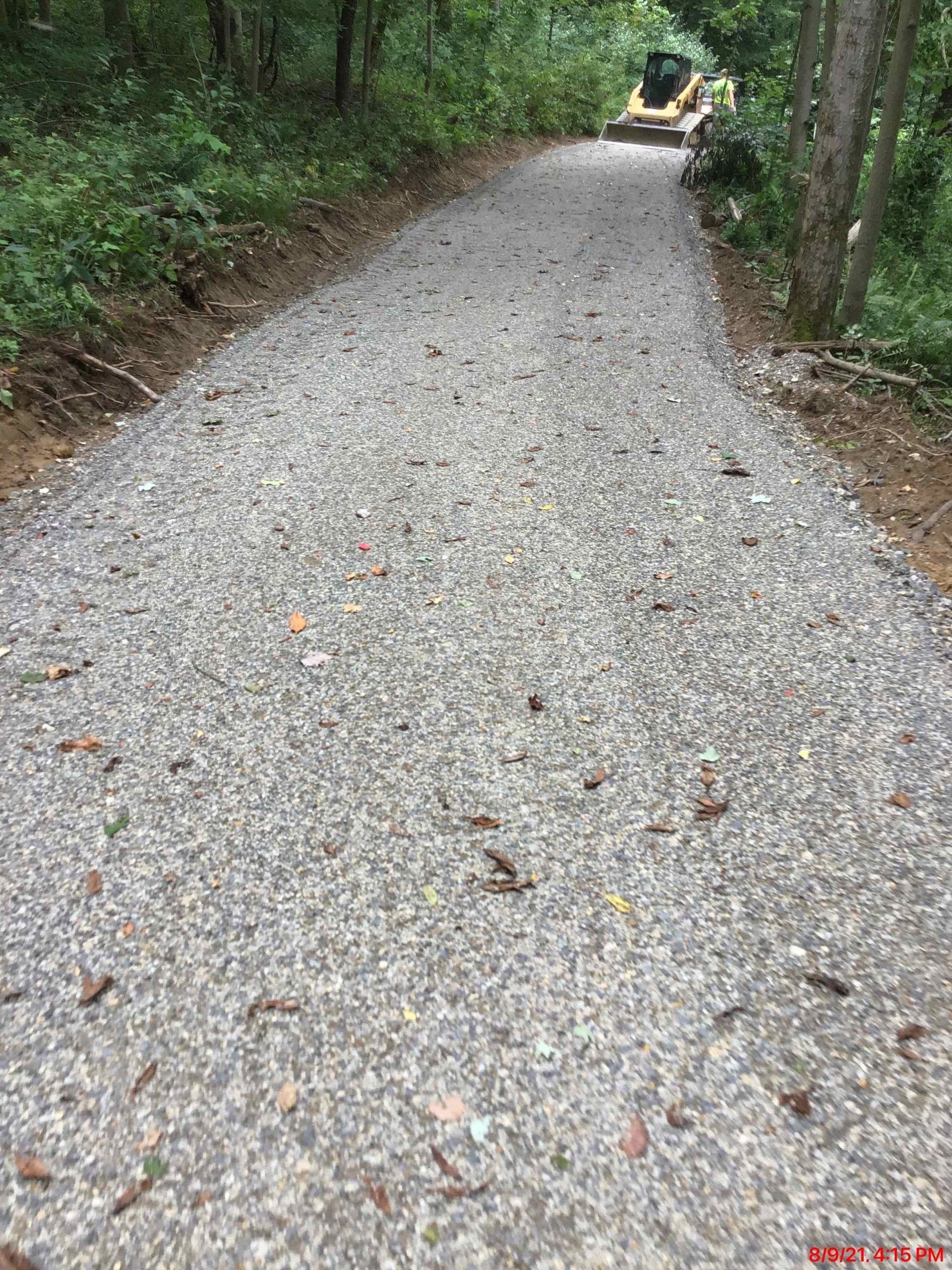 A gravel road in the woods with a bulldozer in the background.